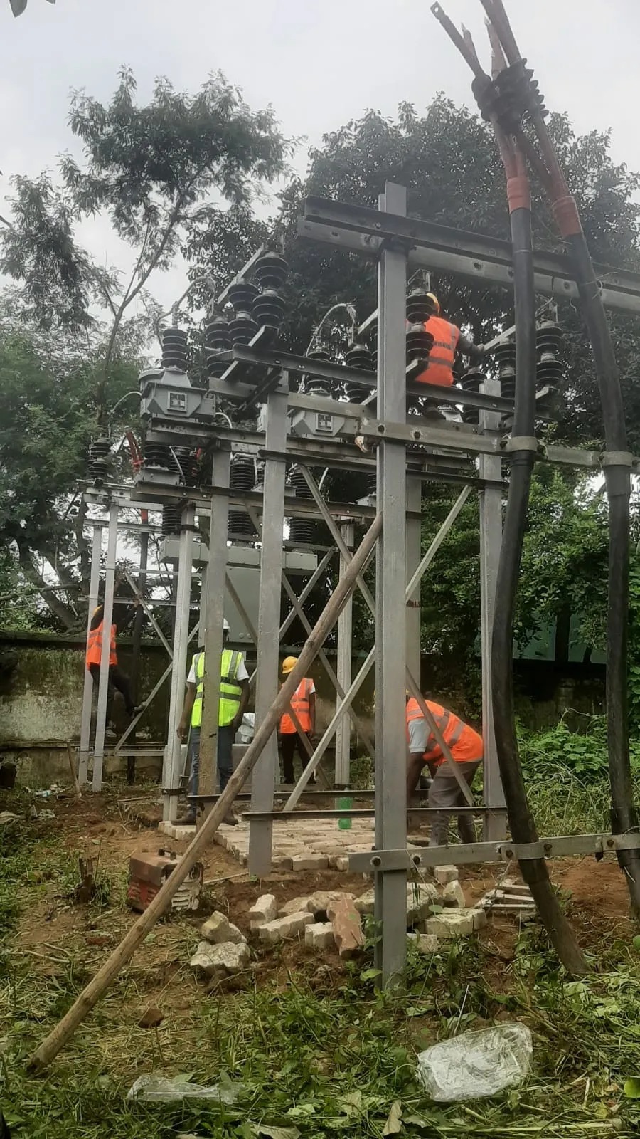 Worker on a cross-arm above mounted switchgear, crew working below