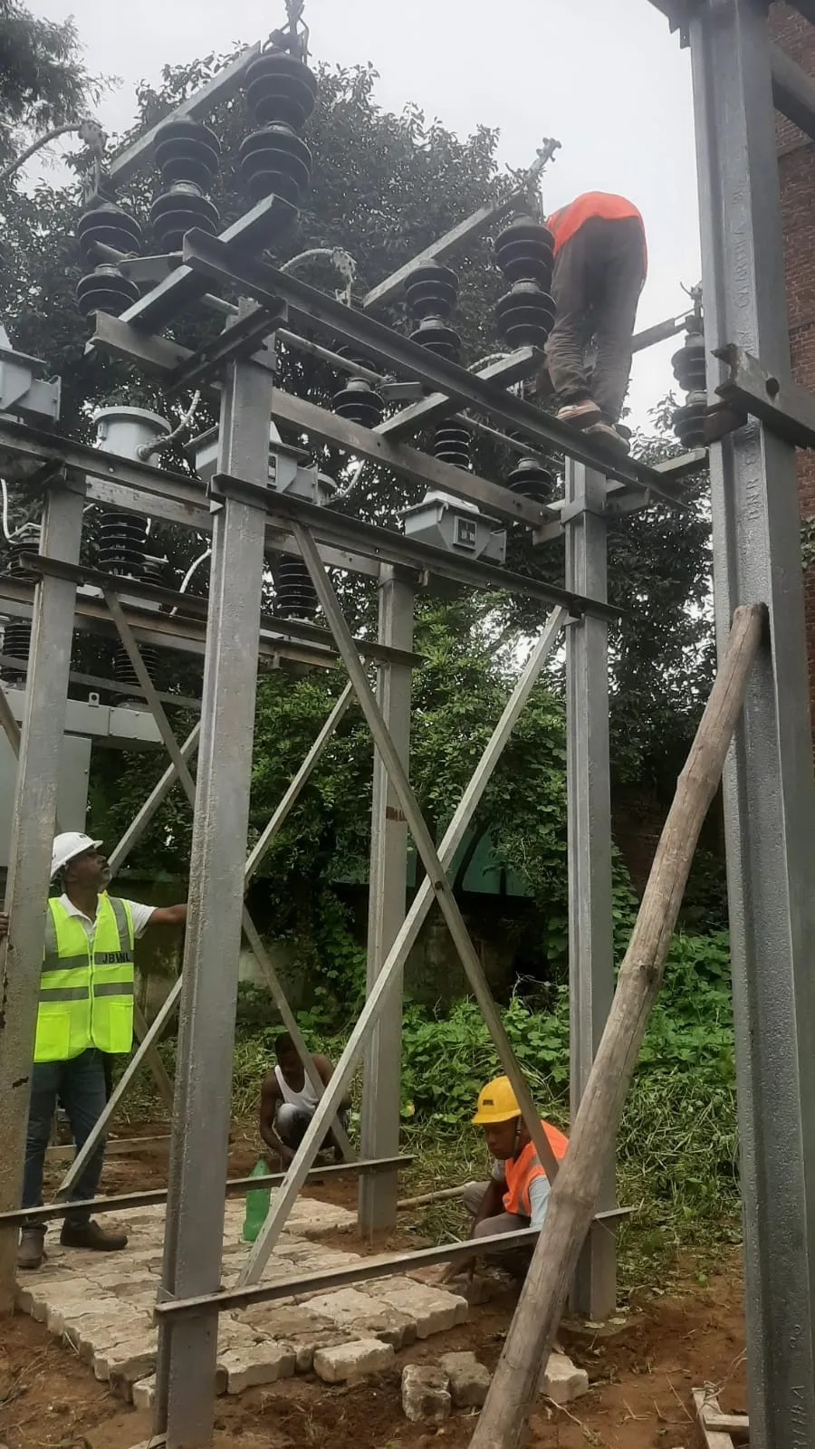 Crew in high-visibility vests and helmets erecting a steel gantry structure in a substation yard