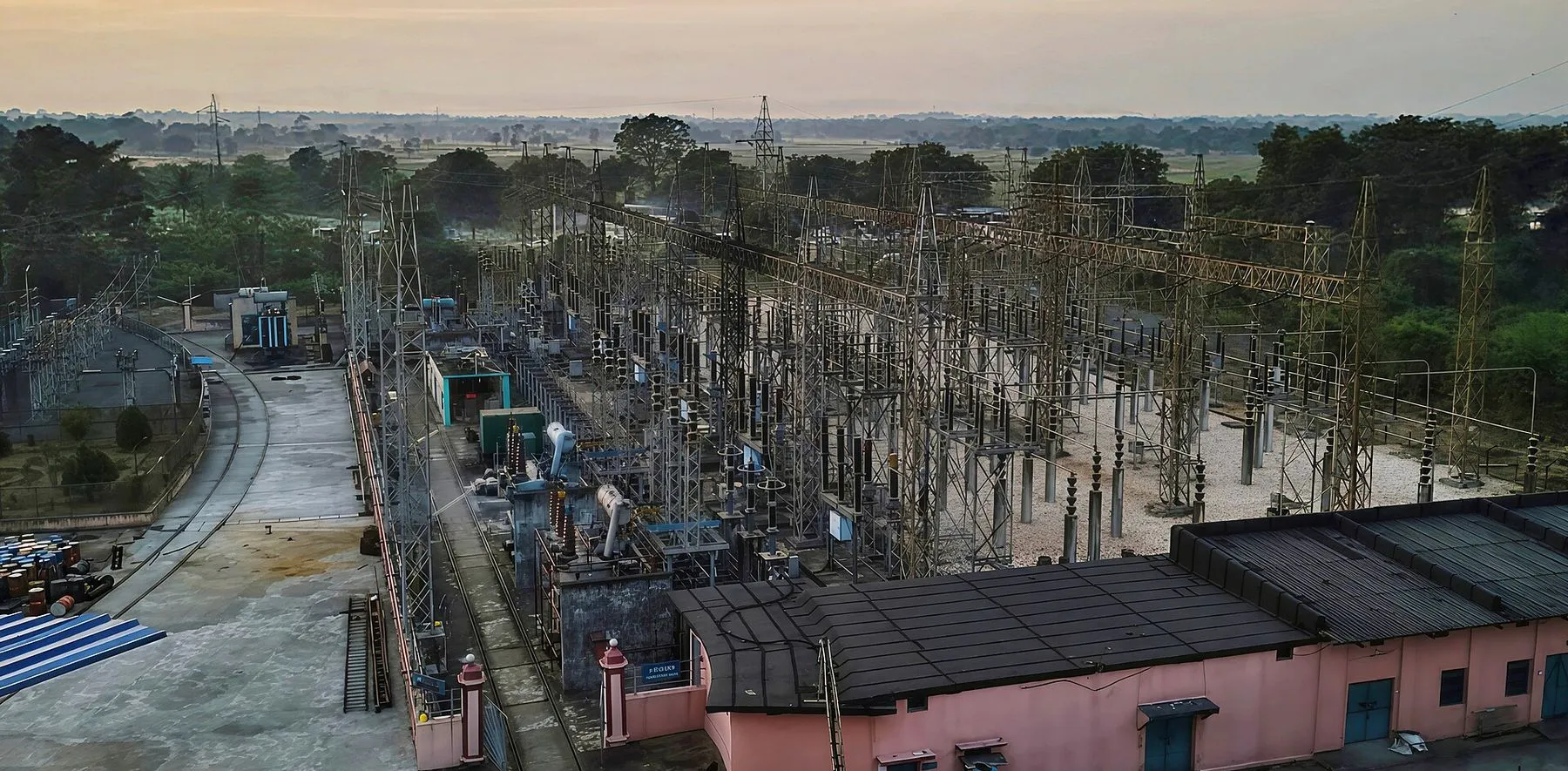 A grid substation switchyard at dawn, with gantries, bus structures and a control building