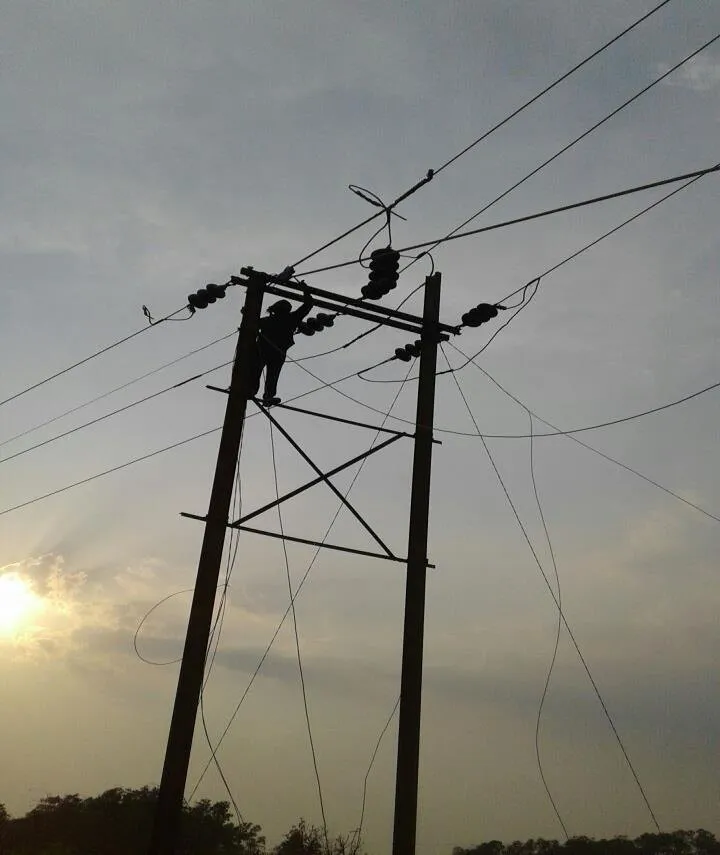 A lineman working at the top of an HT pole against a sunset sky