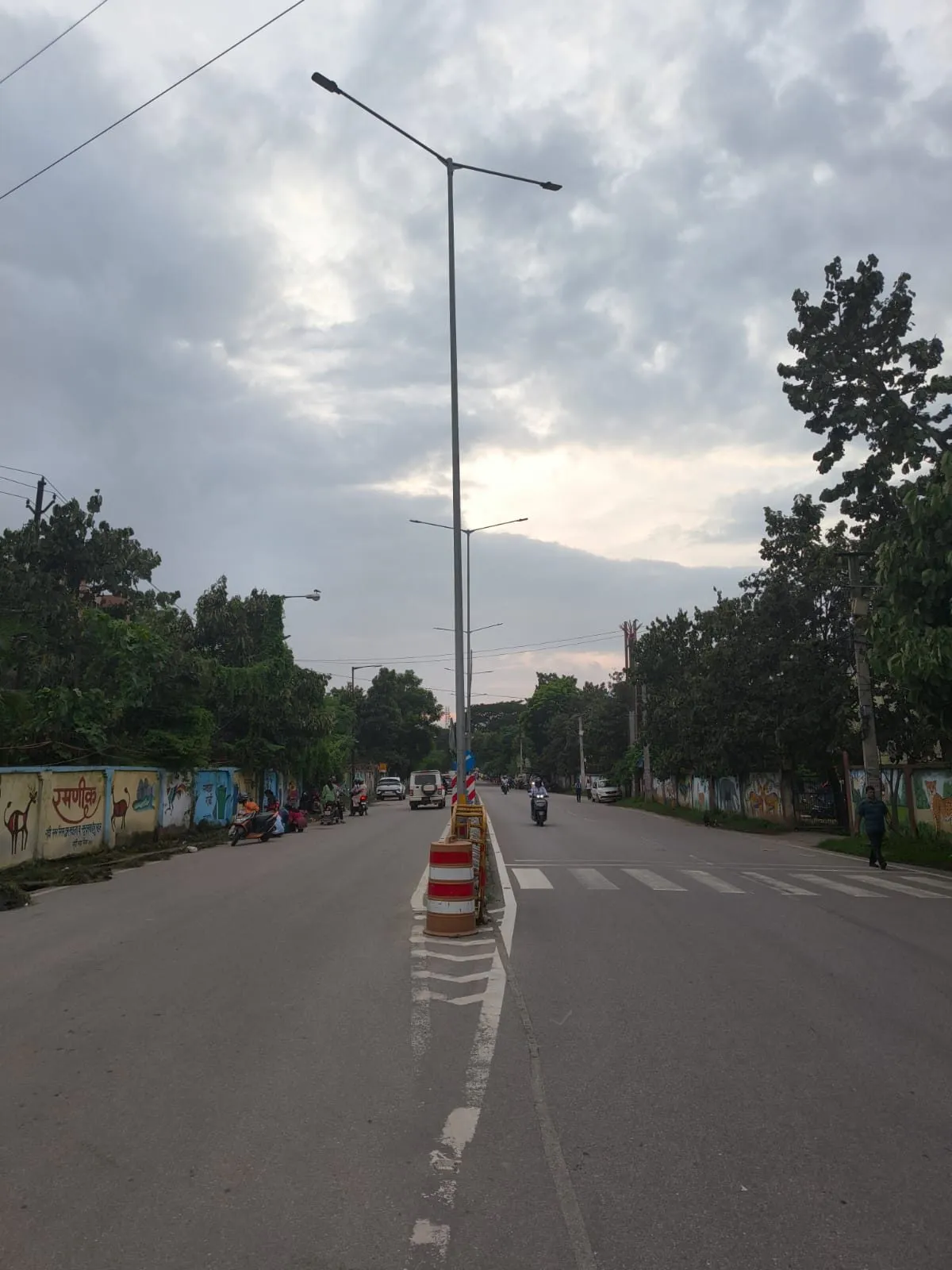 Street lighting pole with a twin-arm luminaire over a divided urban carriageway