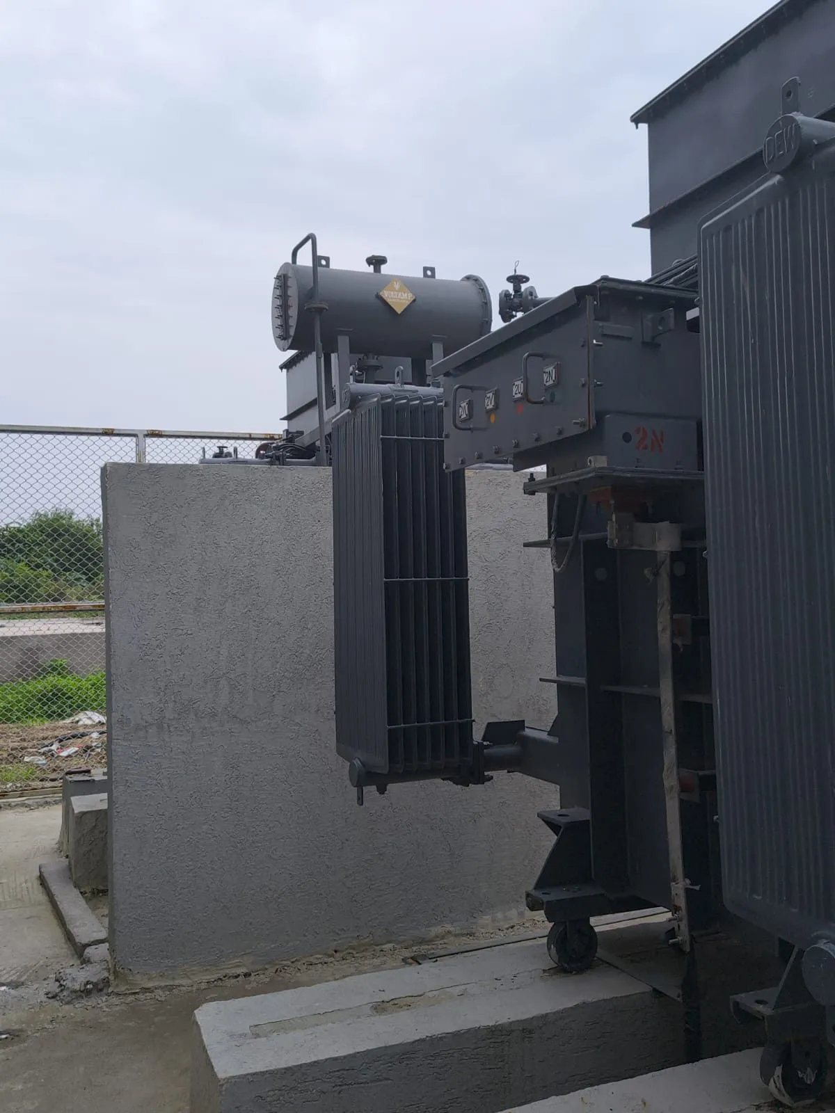 Transformer in its bay seen from the yard, with the boundary fence behind