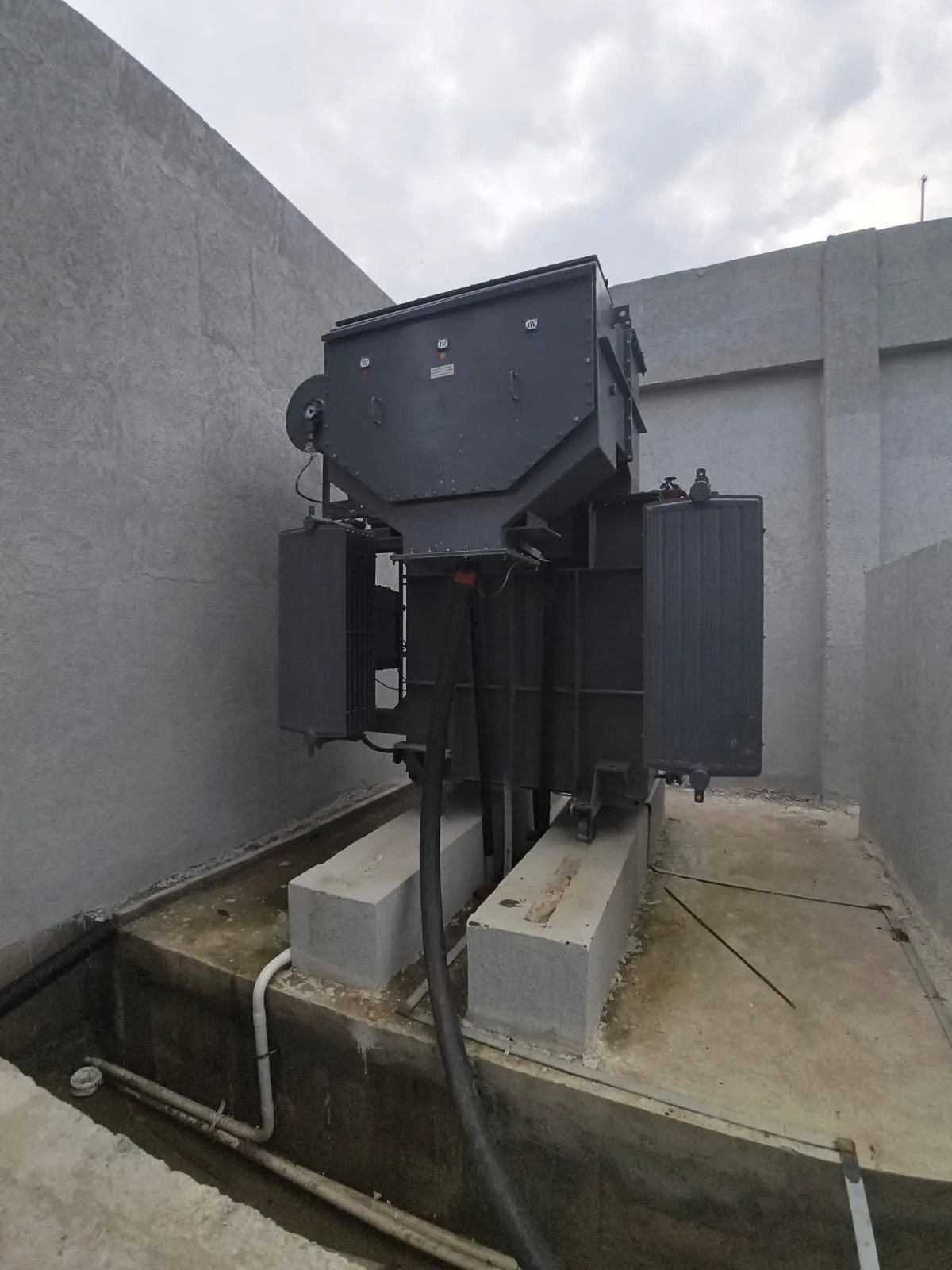 Oil-filled distribution transformer set on a concrete plinth inside a walled bay